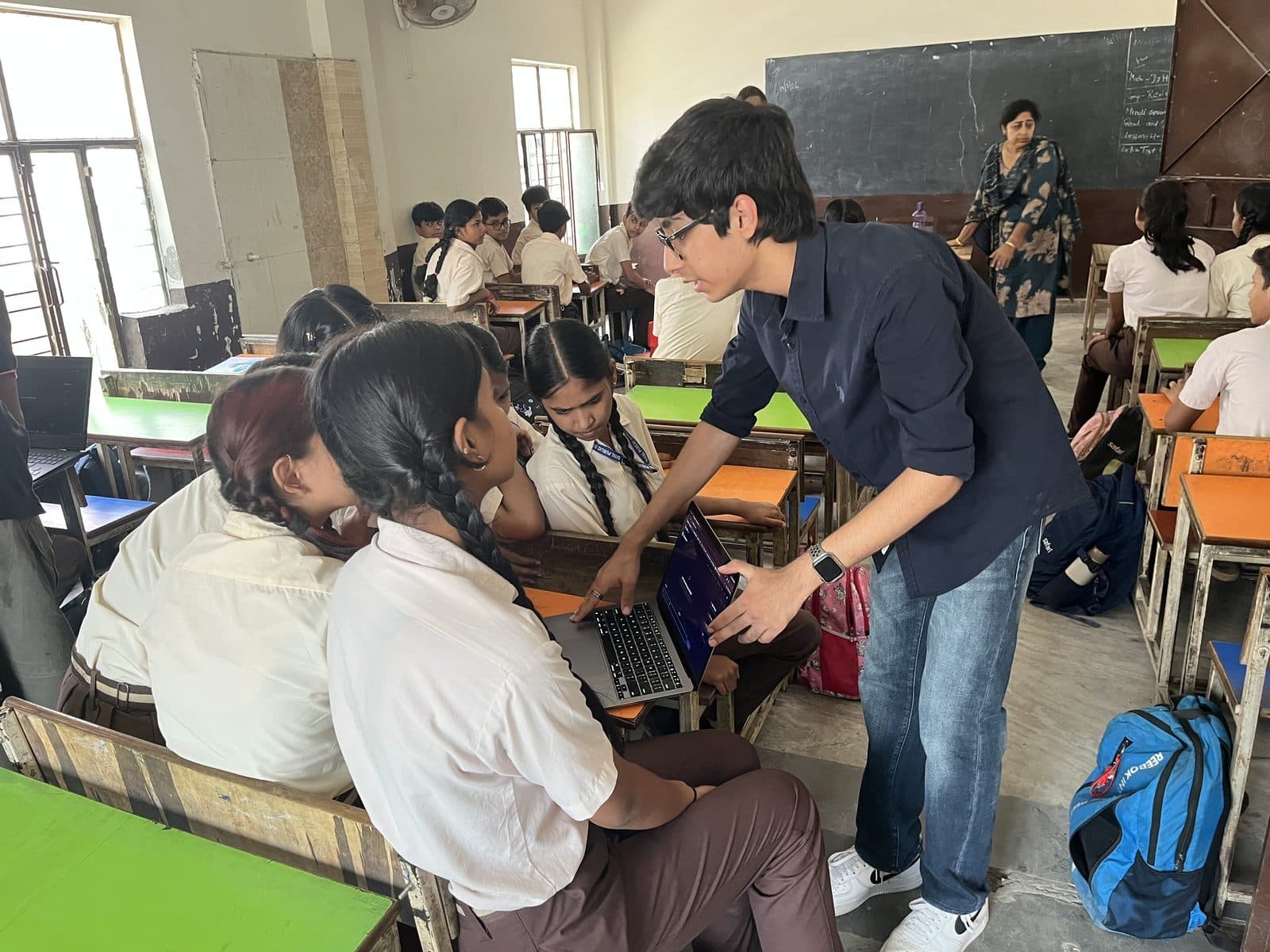 A member of the Edugram team leaning over a desk to show two students the Edugram site on a laptop.