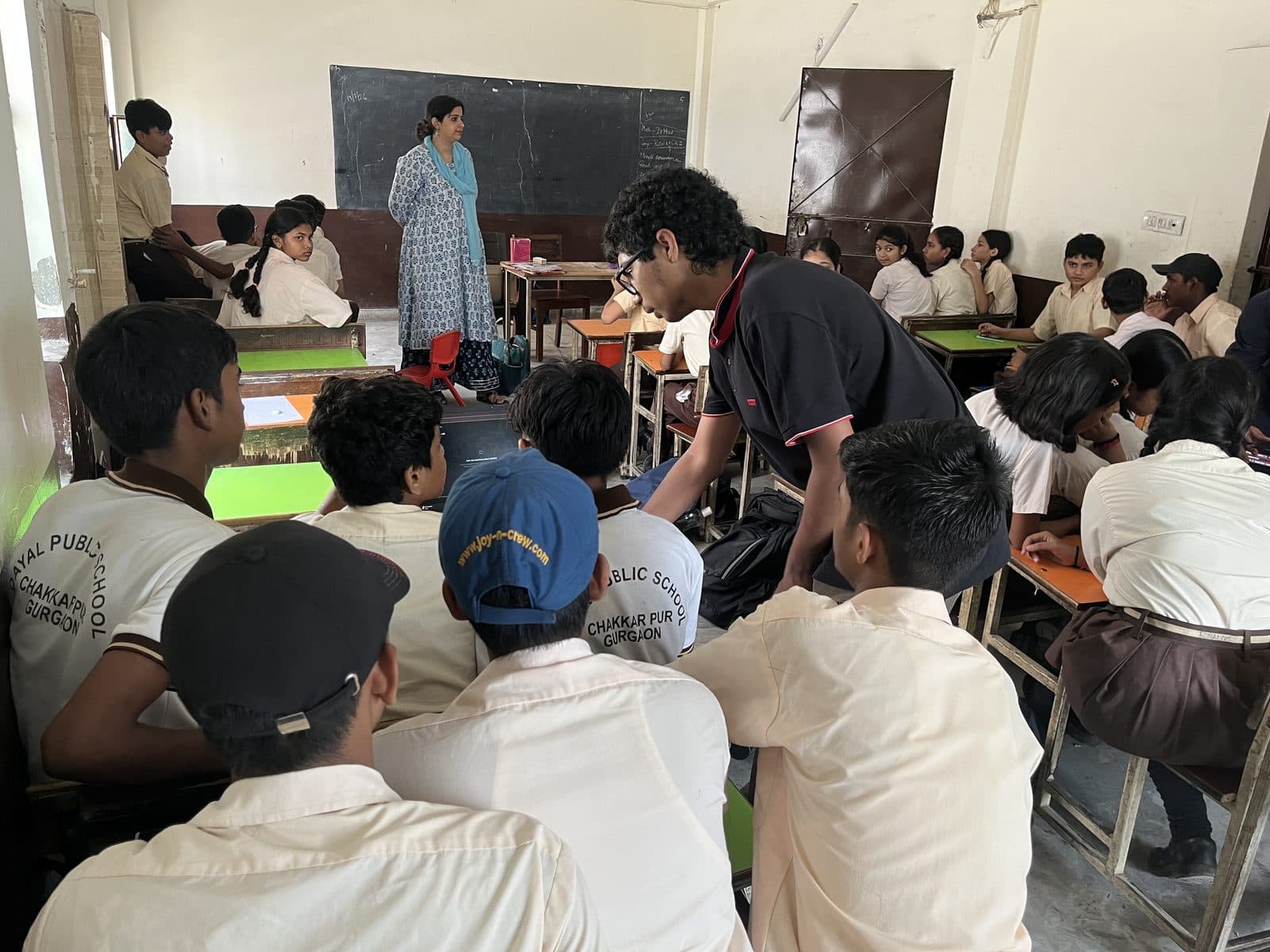 A member of the Edugram team with a cluster of students at their desks, a laptop open between them.