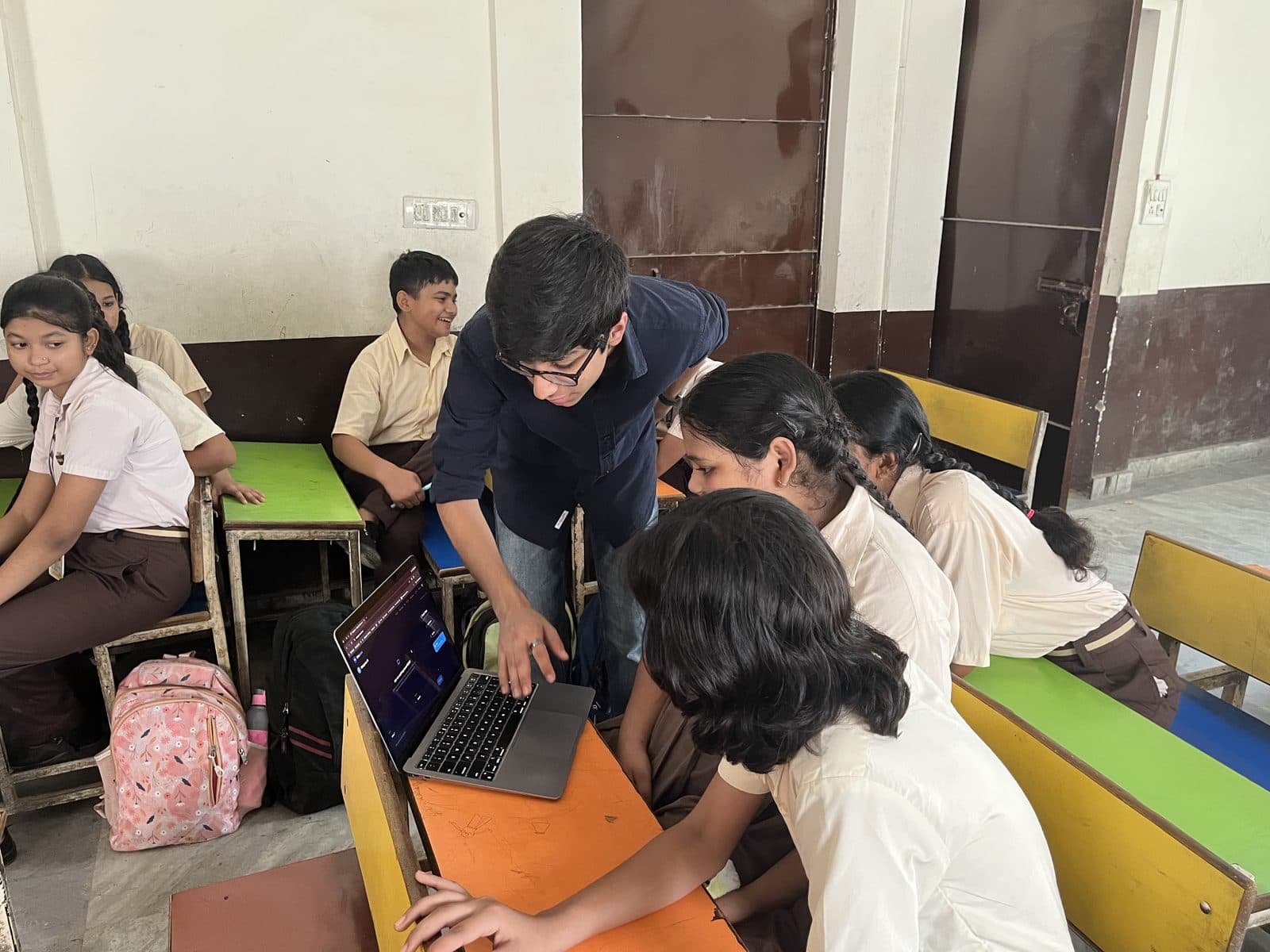 A member of the Edugram team leaning across a desk to a laptop while students on both sides watch the screen.
