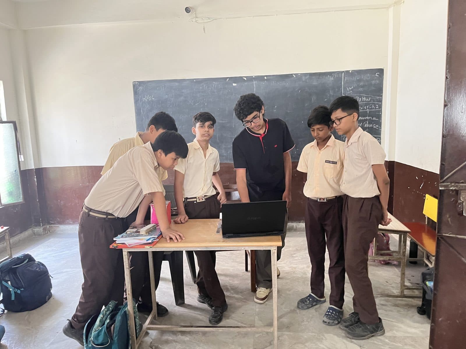 A group of uniformed students standing around a laptop with a member of the Edugram team at Dayal Public School.