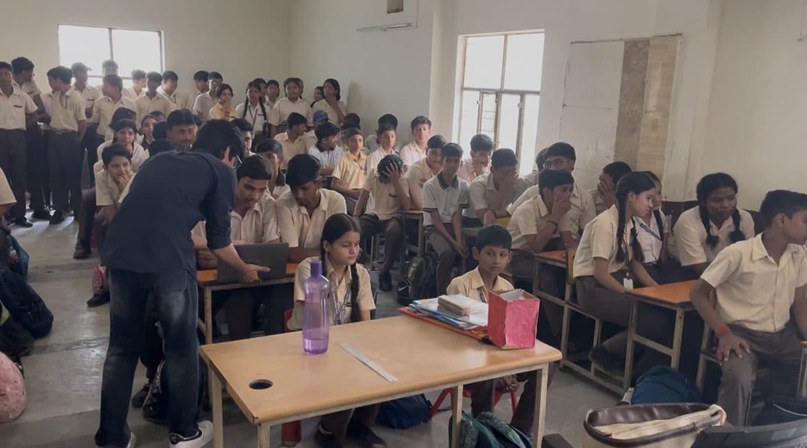 A packed classroom at Dayal Public School, students filling every desk and standing at the back, with a member of the Edugram team at a laptop.