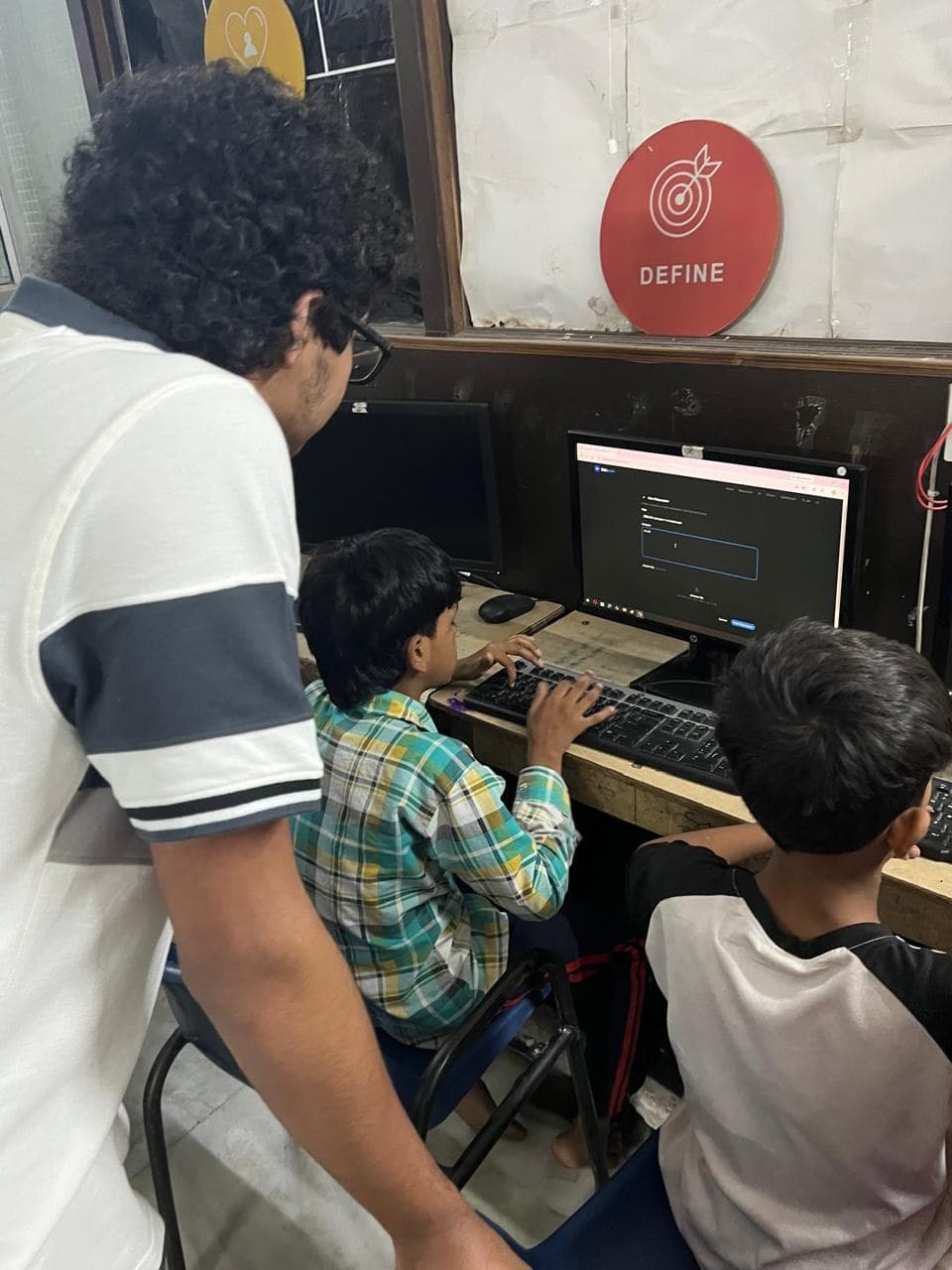 A member of the Edugram team standing beside two boys at Prayatna's computer lab as one of them types a forum post into Edugram.